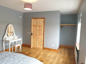 A bedroom with a wooden door, a white dresser with a mirror, and a bed with a patterned bedspread. - Hillside House (Clifden)