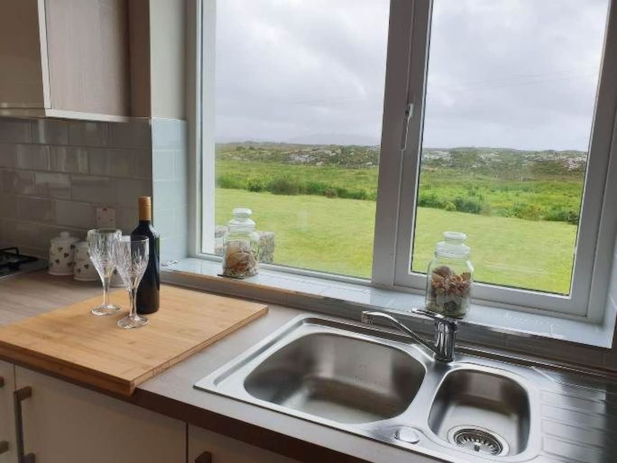 Una cocina con un amplio ventanal, encimera de madera, un lavamanos y una botella de vino.