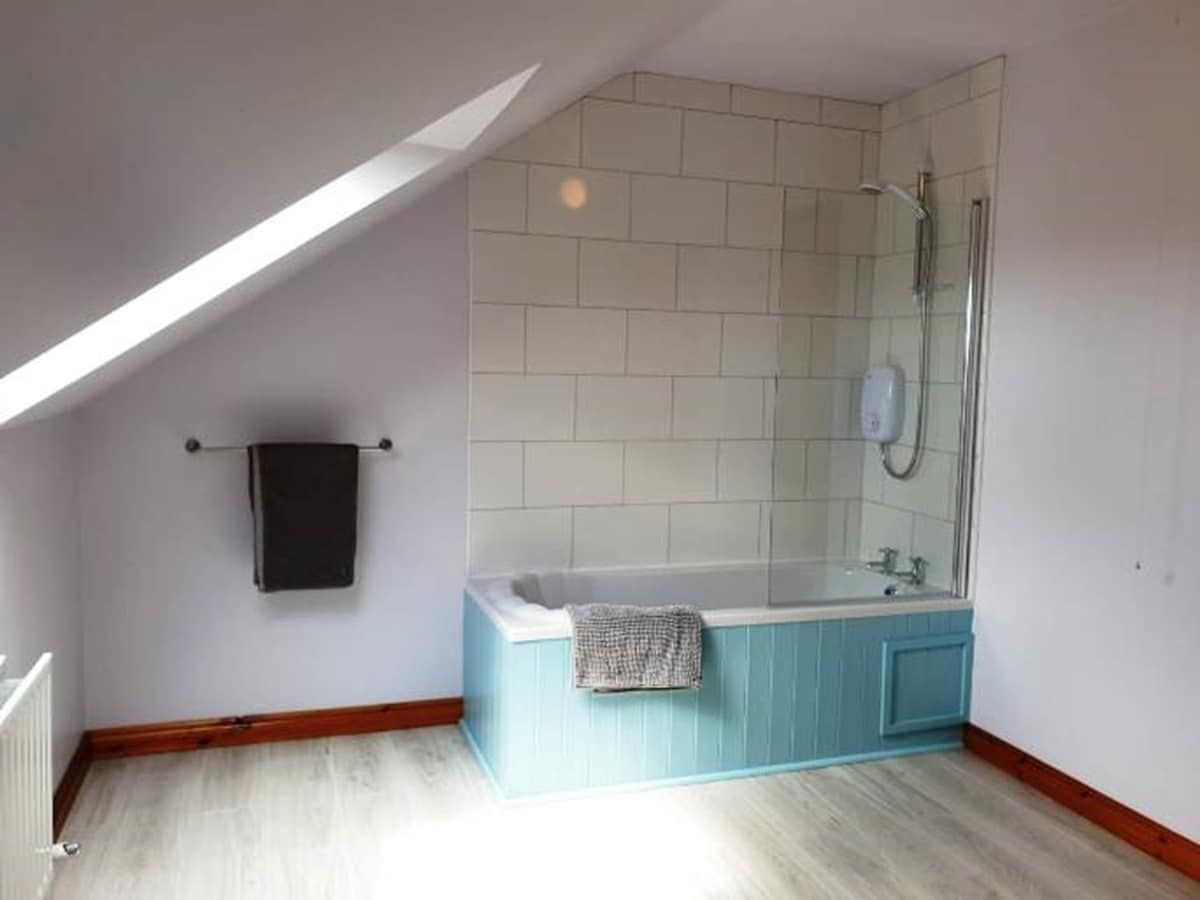 Una habitación con techo inclinado, una bañera y una ducha.