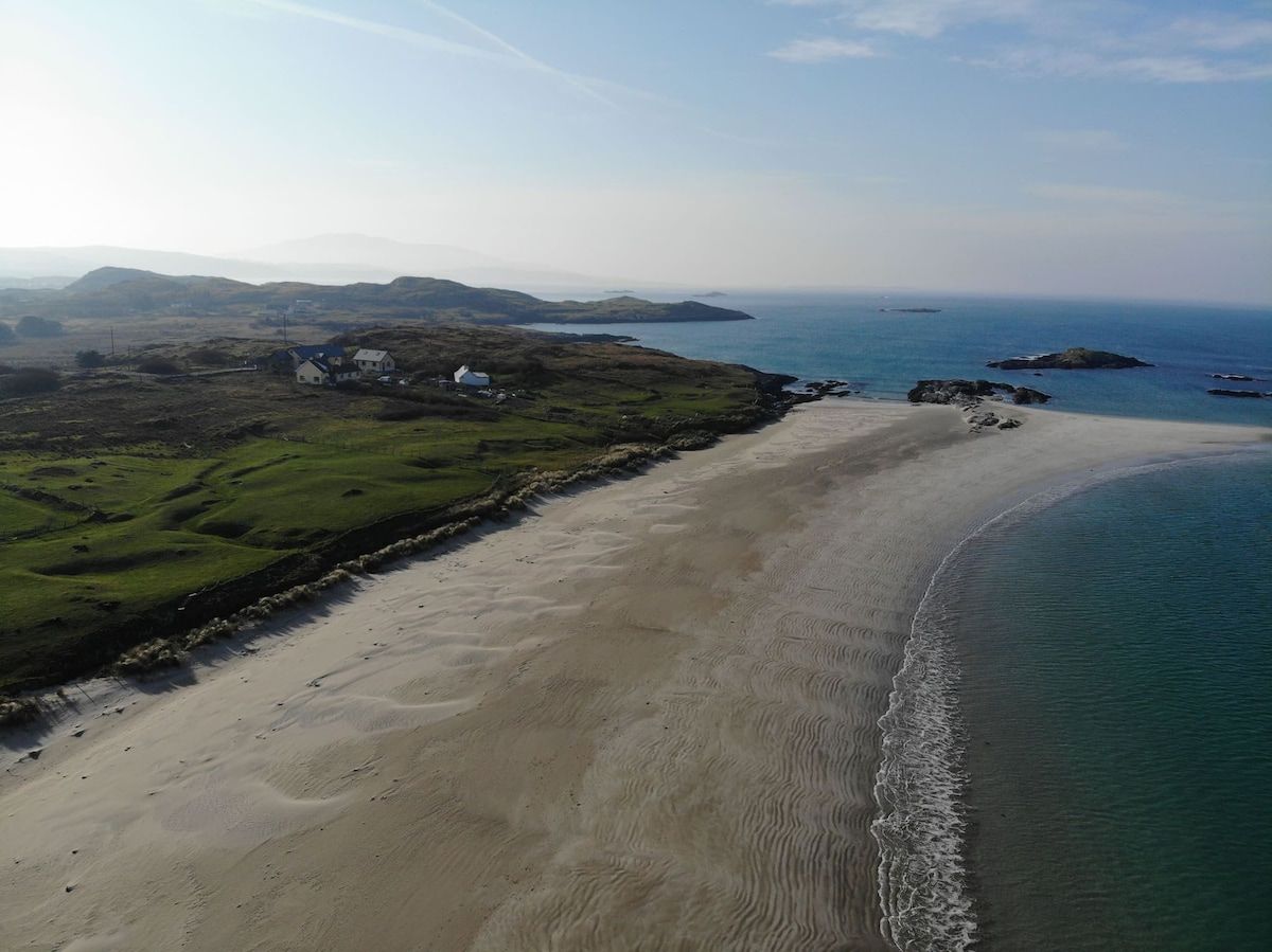 Eine Luftaufnahme einer Küstenlandschaft mit Sandstrand, grünen Flächen und einigen Gebäuden.
