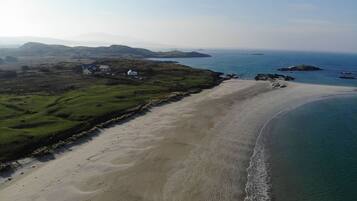 An aerial view of a coastal landscape with a sandy beach, grassy areas, and a few buildings.