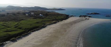 Eine Luftaufnahme einer Küstenlandschaft mit Sandstrand, grünen Flächen und einigen Gebäuden.