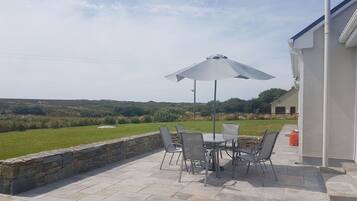 An outdoor patio with a table and chairs, a white umbrella, and a view of the countryside.