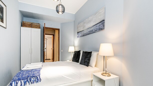 Un dormitorio con una cama grande, lámparas de noche, una mesita de noche pequeña y un cuadro en la pared.