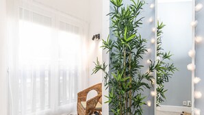 Una habitación con piso a cuadros, una silla de mimbre, una planta de bambú y un espejo con luces.