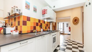 Una cocina con piso a cuadros, gabinetes blancos, salpicadero de azulejos y una ventana con cortinas.