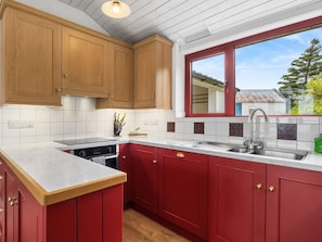 A kitchen with red cabinets, a white countertop, and a window with a view of the outside.