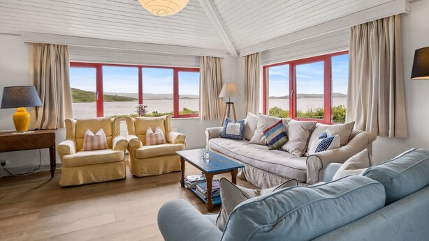 Een ruime woonkamer met uitzicht op zee, met twee banken, een bijzettafeltje en een lamp.