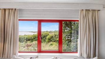 Ein Schlafzimmer mit großem Fenster, einem Bett mit Kissen und Vorhängen.