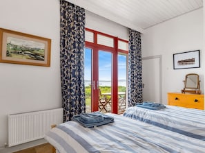 A bedroom with a bed, a dresser, a window with curtains, and a view of the outdoors.