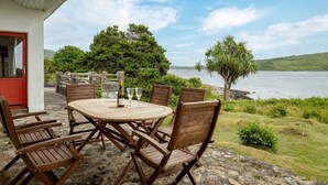 Een terras buiten met een ronde tafel en stoelen, met uitzicht op een waterpartij en groen.