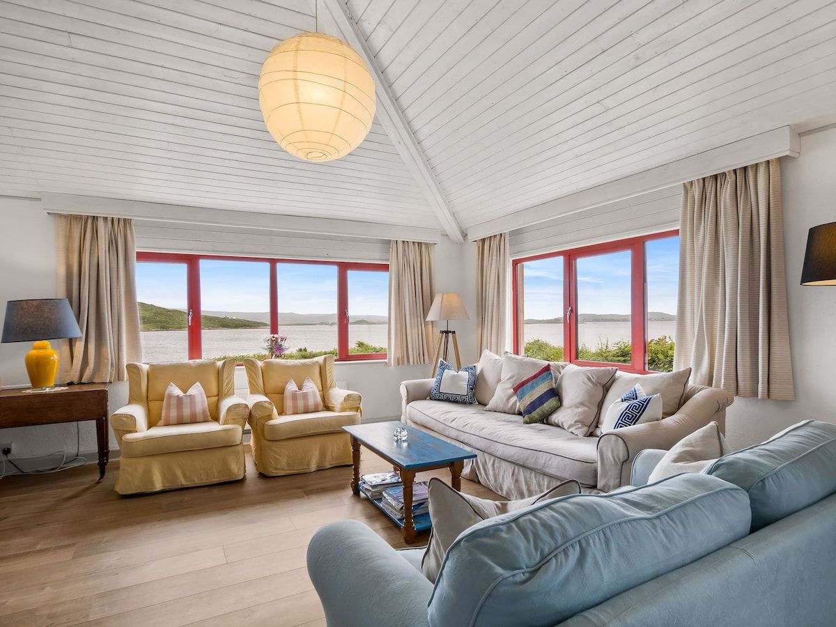 Un salón amplio con techo alto, ventanas grandes y vista al mar.