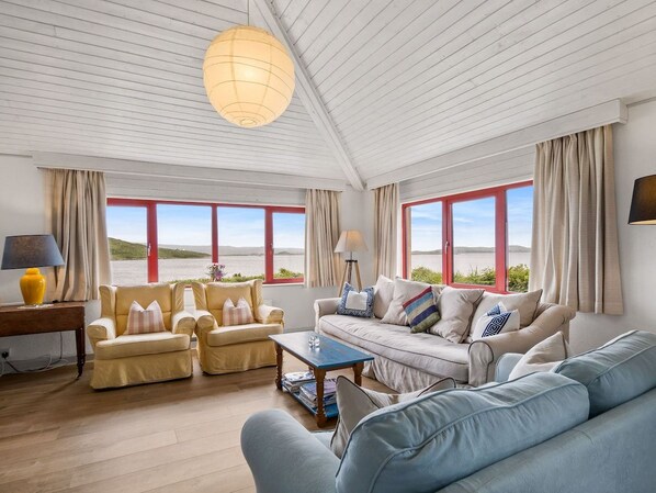 A spacious living room with a high ceiling, large windows, and a view of the sea.
