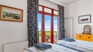 Een slaapkamer met een bed, een dressoir, een spiegel en een raam met gordijnen.