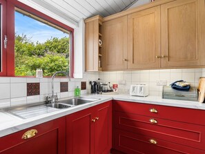 A kitchen with red cabinets, a white countertop, and a window with a view of greenery.