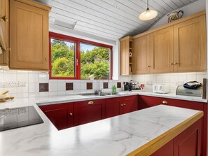 A kitchen with a large island, red cabinets, a window with a view, and a white countertop.