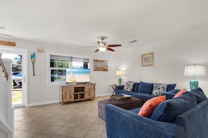 A living room with a TV, a ceiling fan, a window with a view, a wooden cabinet, and a blue sofa.