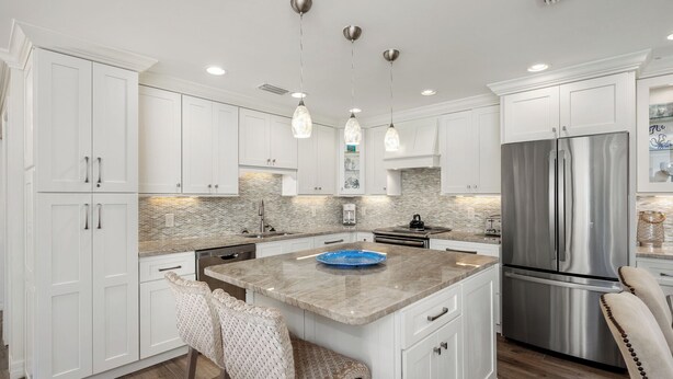 A modern kitchen with white cabinetry, a central island, stainless steel appliances, and pendant lighting. - Gorgeous Partial Beach View 3 bed, 2 bath at Sanibel Moorings #532 (Sanibel)