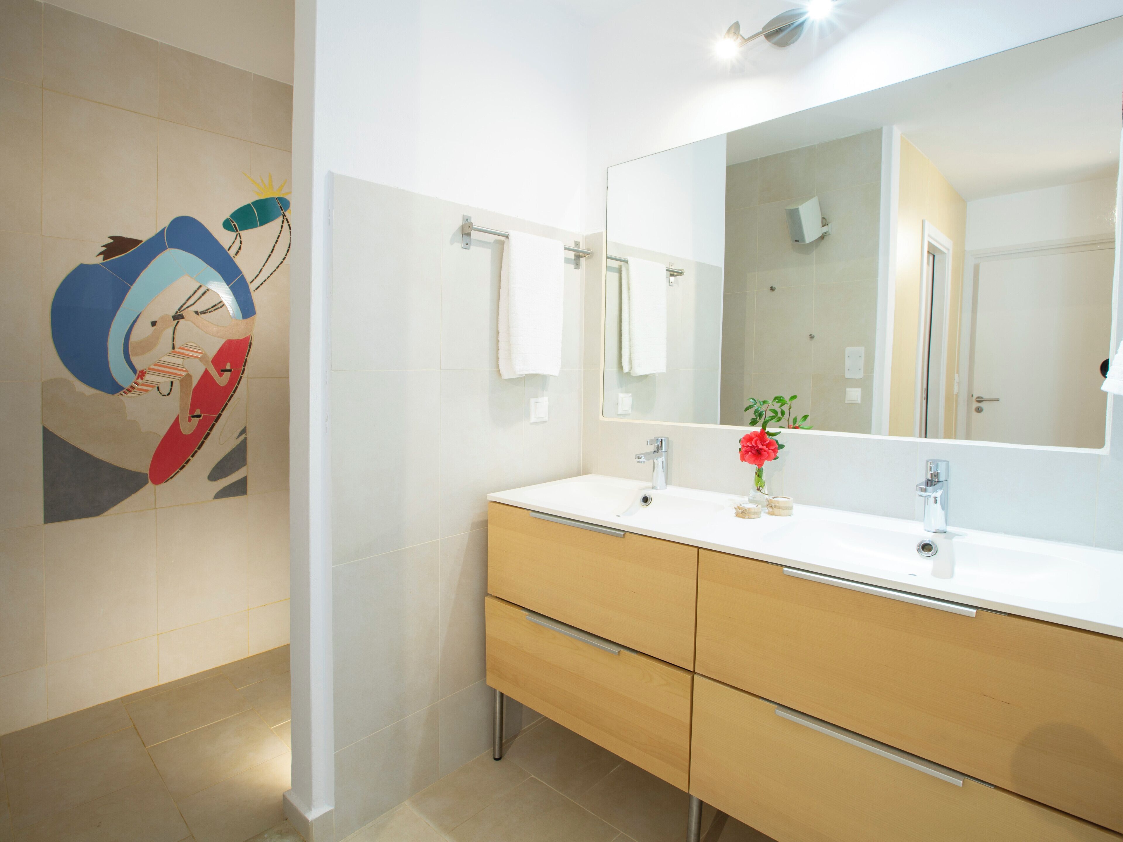A modern bathroom with a large mirror, two sinks, and a wooden vanity.