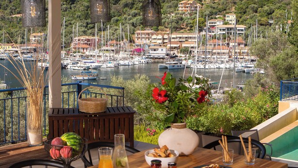 A terrace with a table set for breakfast overlooking a marina with boats and buildings. - Villa Sivota, Exclusive sea front Villa with 99" Underground Cinema (Sivota)