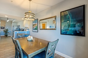 A dining area with a wooden table, chairs, a hanging light fixture, and framed artwork on the walls. - FFR110 - Nautical Twilight by First Flight Rentals (Kill Devil Hills)
