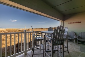 A covered outdoor seating area with a view of the beach, a table, and chairs.