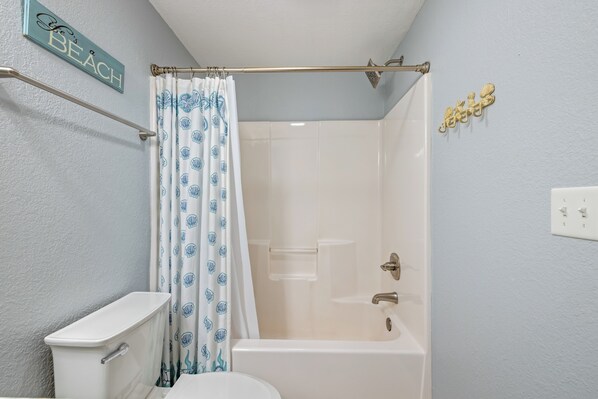 Un baño con inodoro, bañera, cortina de ducha y barra para toallas.