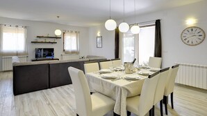 A dining area with a table set for four, a kitchen in the background, and a large wall clock. - Comfortable villa just 1,5 km from beach with private pool (Medulin)