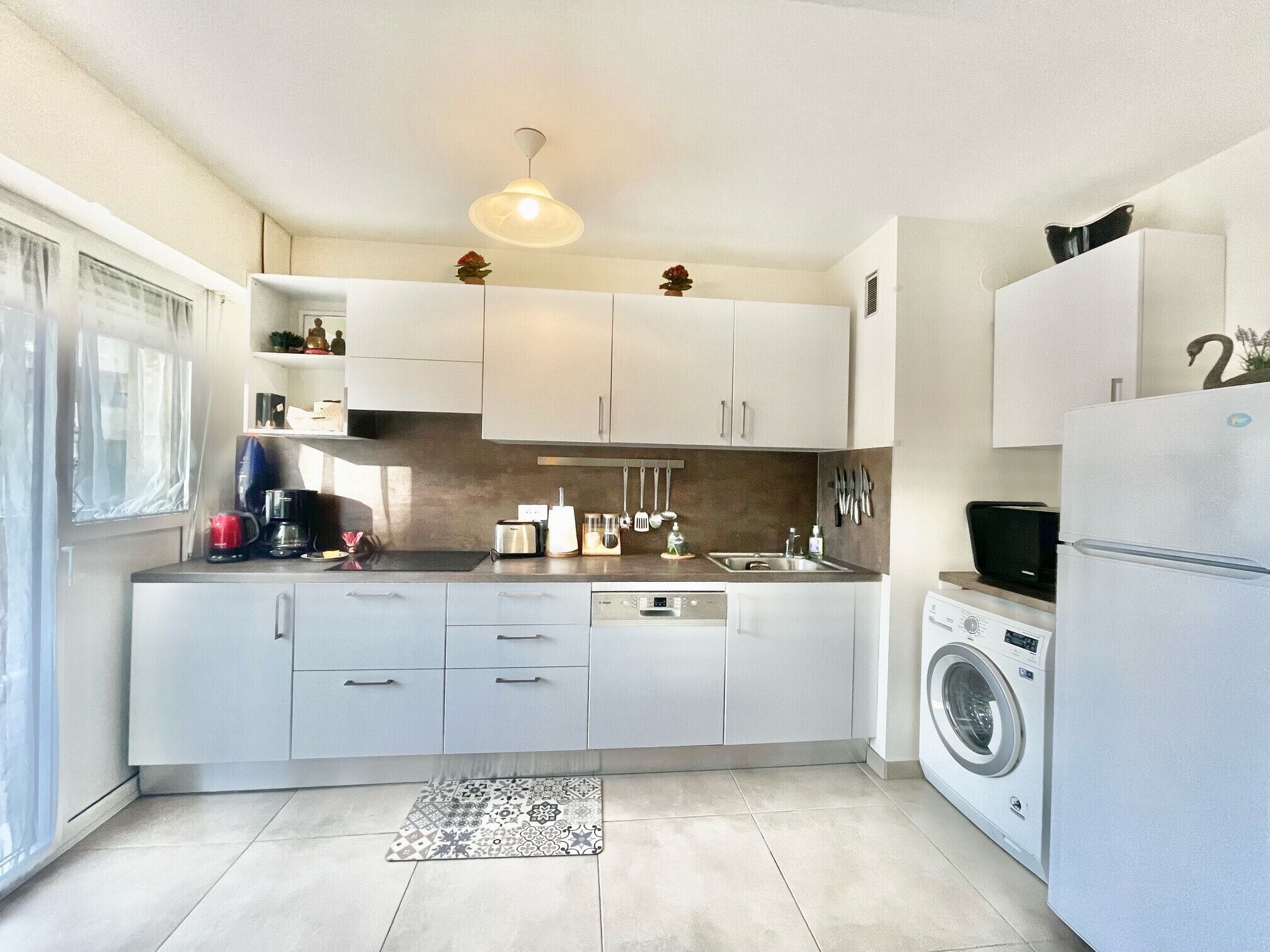 Ett modernt kök med vita skåp, en inbyggd tvättmaskin och en kaffebryggare.