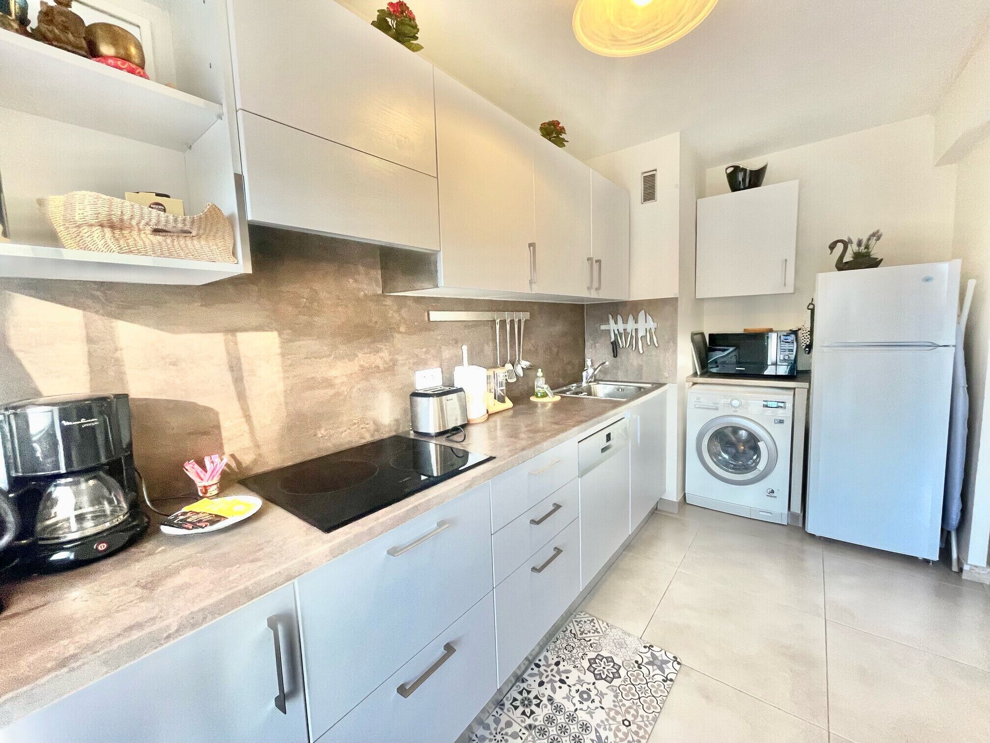 A modern kitchen with white cabinets, a built-in oven, a microwave, a sink, and a washing machine.