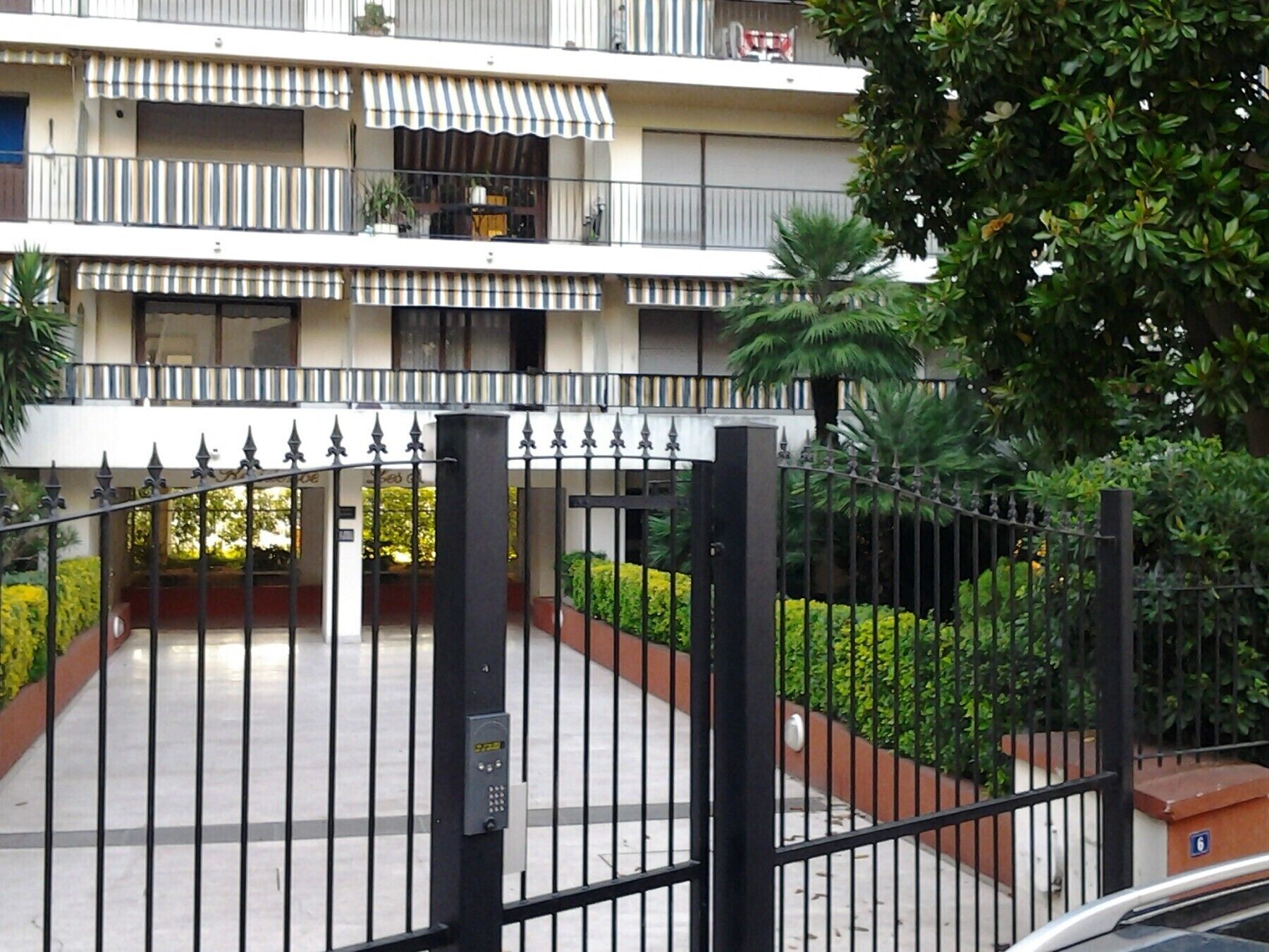 Una entrada cerrada con portón de metal y teclado electrónico a un edificio de diseño moderno.
