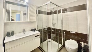 Een moderne badkamer met een douchecabine van glas, een wit wastafelmeubel met spiegel erboven en een toilet.