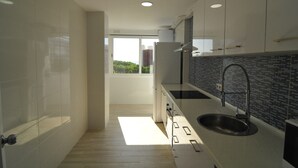 A modern kitchen with white cabinets, a black backsplash, and a large window providing a view of greenery outside. - HomeHolidaysRentals Solmar - Costa Barcelona (Santa Susana)