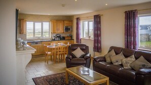 A living room with a leather sofa, a glass coffee table, and a dining area with wooden chairs and a table. - Atlantic Sunset,  Aughris is a home away from home (Cleggan)
