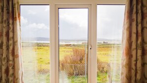 A room with a large window offering a view of a grassy field and a distant building. - Atlantic Sunset,  Aughris is a home away from home (Cleggan)