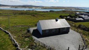 A stone building with a sloped roof, surrounded by a gravel driveway and a stone wall. - Atlantic Sunset,  Aughris is a home away from home (Cleggan)