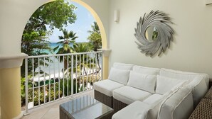 A balcony with a white cushioned sofa, a glass-top coffee table, and a decorative mirror. - Modern Beachfront Condo with Pool - Sapphire 211 (Saint Lawrence Gap)