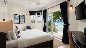 A hotel room with a bed, a desk, a chair, a TV, and a balcony with a view of the ocean. - Modern Beachfront Condo with Pool - Sapphire 211 (Saint Lawrence Gap)