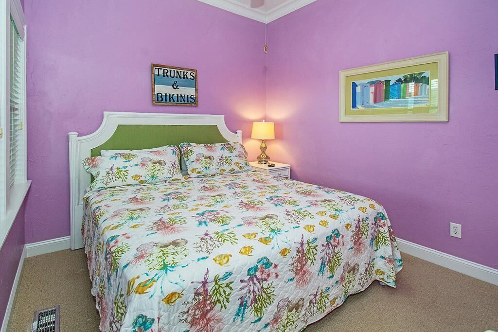 Una camera da letto con una coperta a fiori, un comodino con una lampada e un quadro appeso al muro.