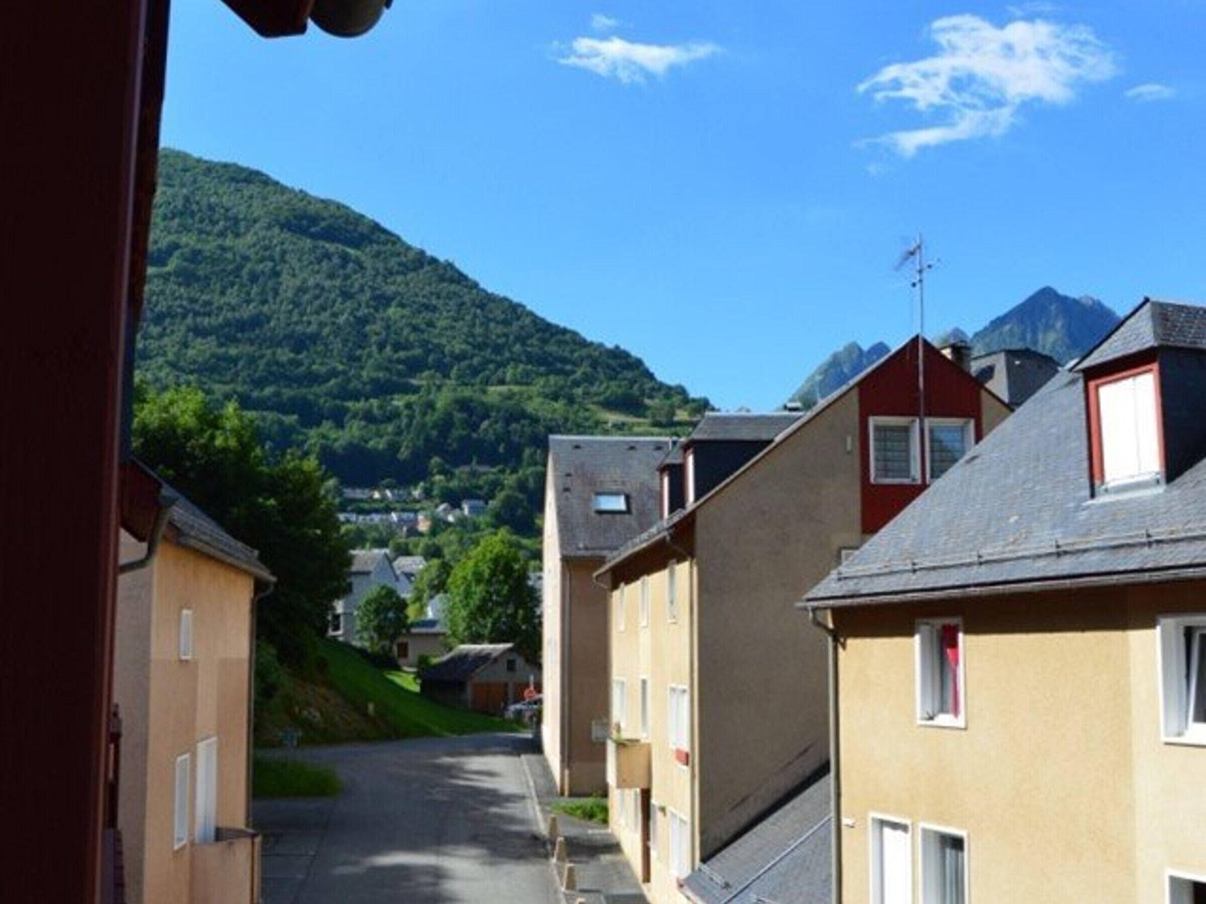 Eine schmale Straße mit Wohnhäusern, ein klarer blauer Himmel und ein Berg im Hintergrund.