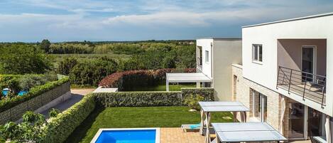 A modern villa with a swimming pool, outdoor seating, and a view of the countryside.