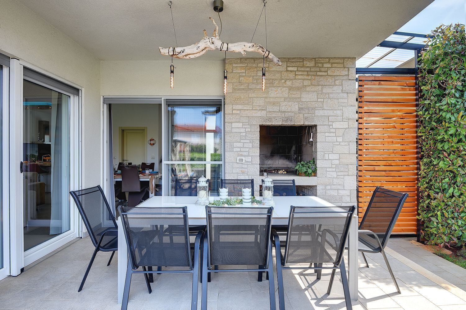 Un espace extérieur aménagé pour les repas, avec une cheminée en pierre, une clôture en bois et une porte vitrée donnant sur un patio.