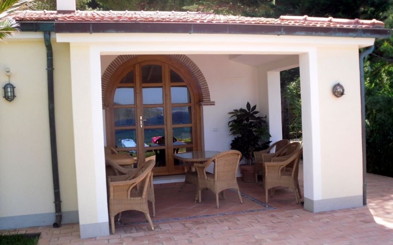 Une terrasse couverte, aménagée avec des meubles en osier et dotée d’une grande fenêtre en arc de cercle.