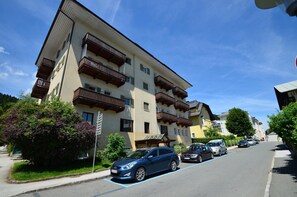 Un edificio a più piani con balconi, auto parcheggiate e aree verdi.