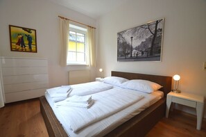 Camera d'albergo con un letto matrimoniale, un comodino con una lampada, un termosifone, una finestra con tende e due quadri appesi al muro.