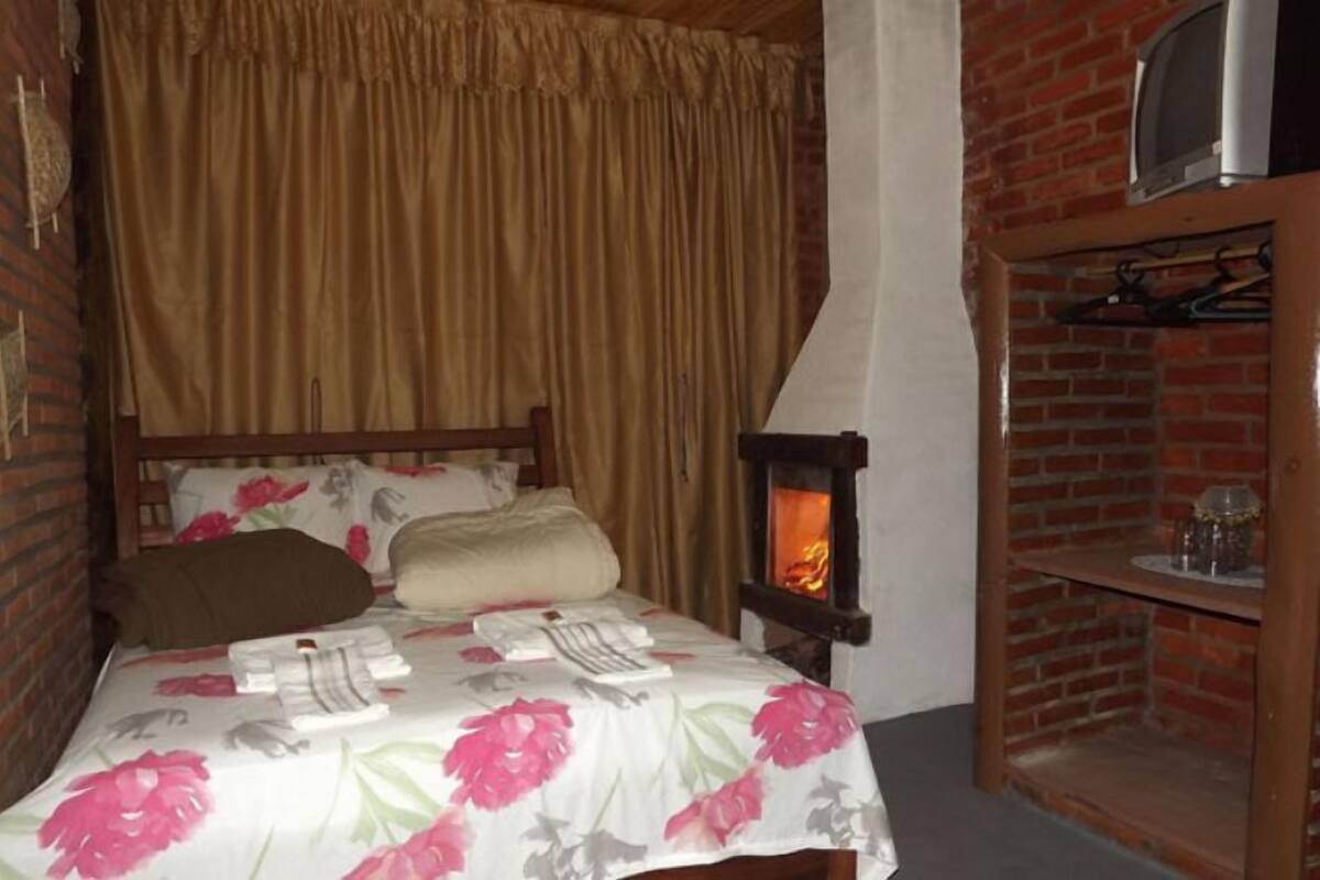 Une pièce chaleureuse avec un lit, une tête de lit en bois, un mur en briques, une cheminée et une étagère avec des verres.