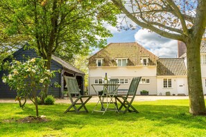 A house with a tiled roof, a small garden with a table and chairs, and a tree in the foreground.