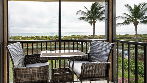 A covered outdoor seating area with wicker furniture and a view of the ocean.