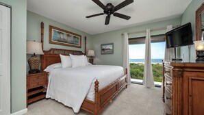 A bedroom with a bed, a ceiling fan, a TV, and a view of the ocean.