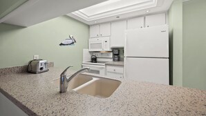 Une cuisine moderne dotée d’un plan de travail en granit, d’un évier en acier inoxydable, de meubles blancs, d’un four à micro-ondes, d’une machine à café et d’un réfrigérateur Whirlpool.
